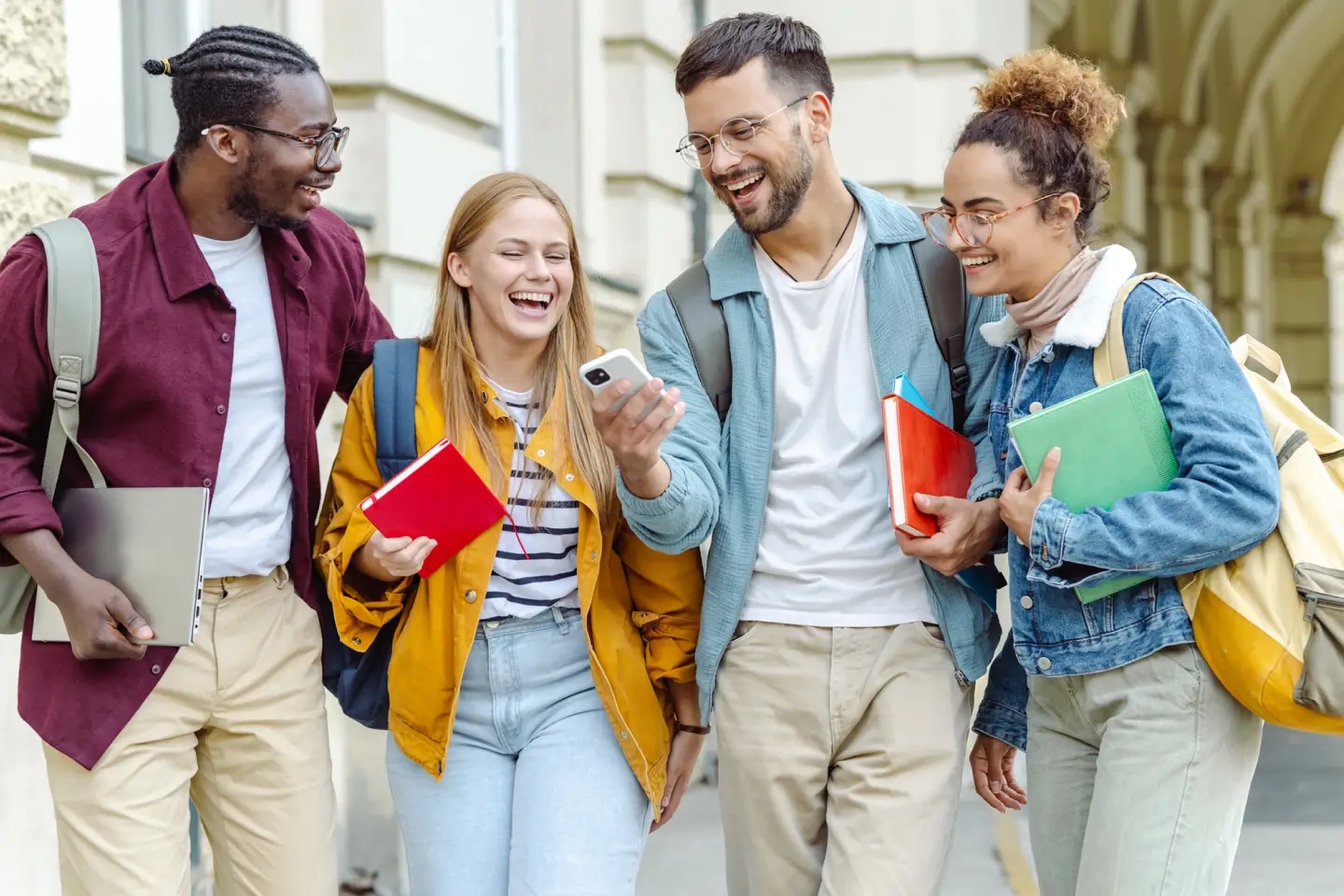 four students holding books while walking down the street
